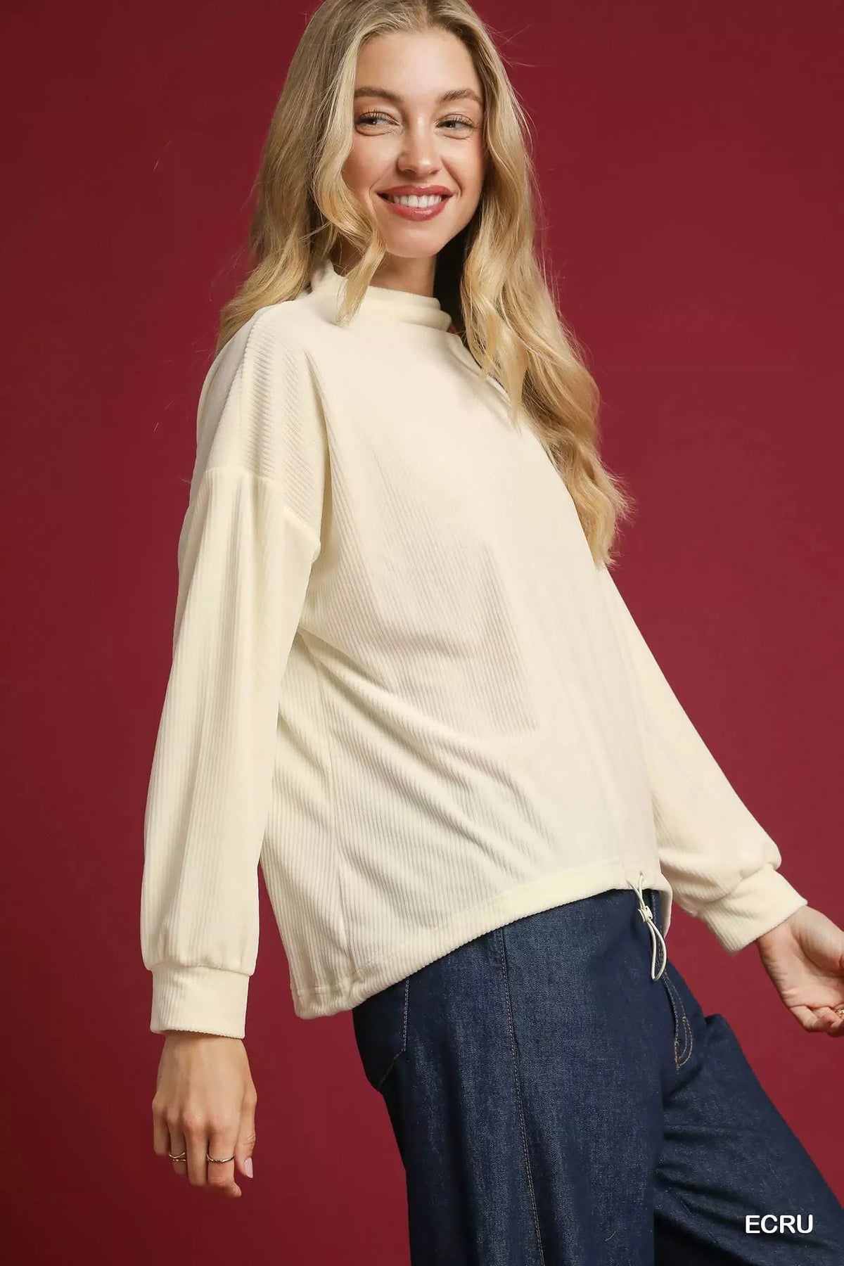 Woman wearing an ecru ribbed long sleeve top with relaxed fit and dark denim pants