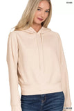 Woman wearing a light beige hooded sweatshirt with drawstrings and blue jeans