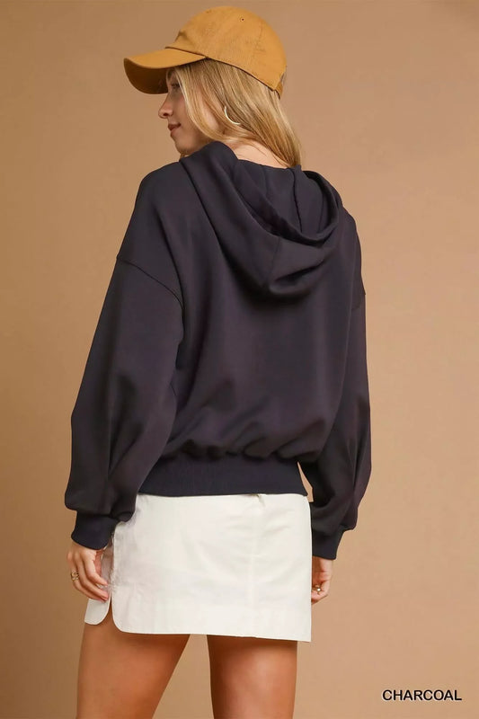 Woman in charcoal hooded sweatshirt, white mini skirt, and tan cap, back view