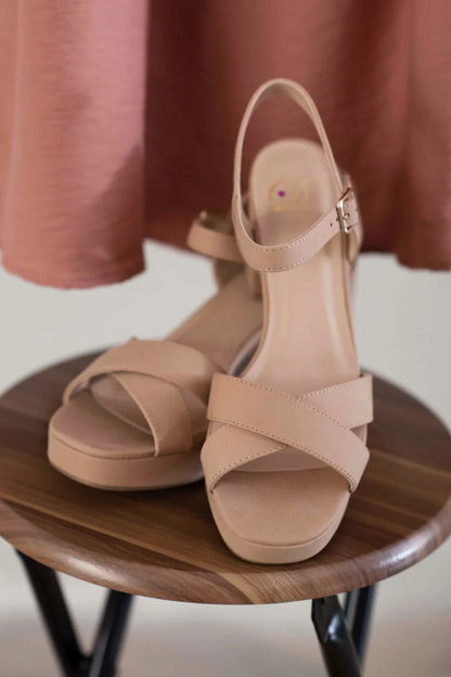 Beige platform sandals with ankle strap and crisscross front on a wooden stool