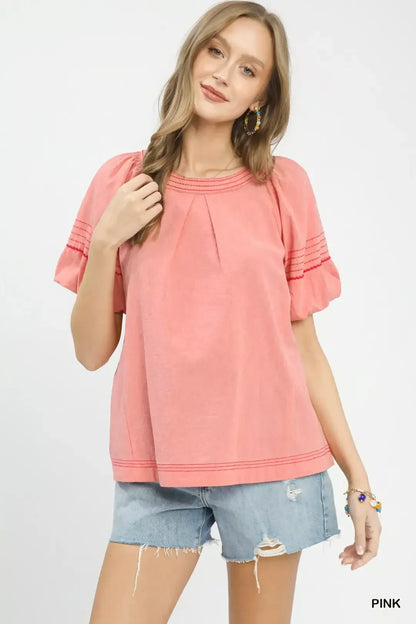 Woman wearing a pink short-sleeve blouse with ruched details and denim shorts.