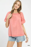 Woman wearing a pink short-sleeve blouse with ruched details and denim shorts.