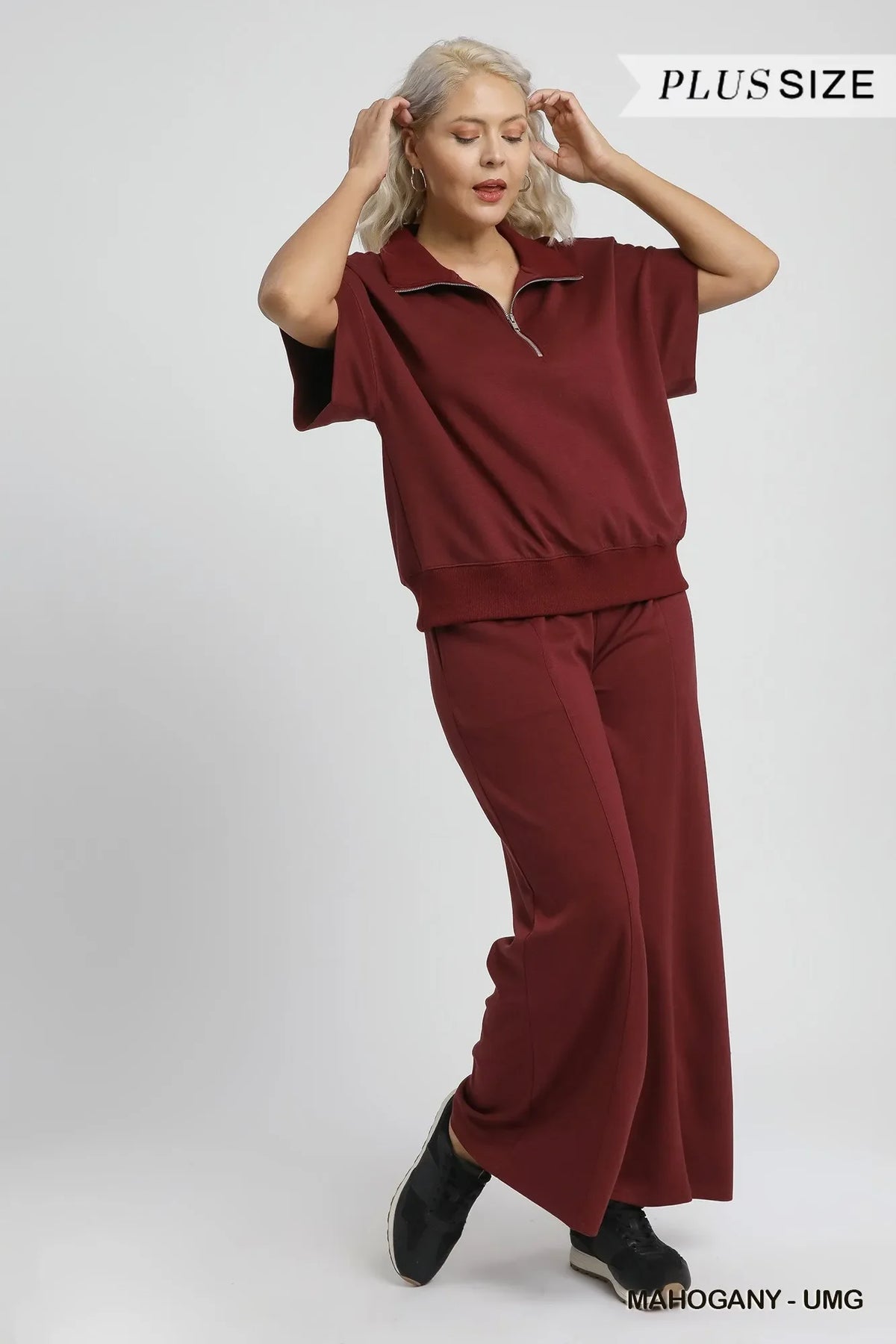 Plus size woman wearing relaxed fit mahogany lounge set with zip collar and wide-leg pants.