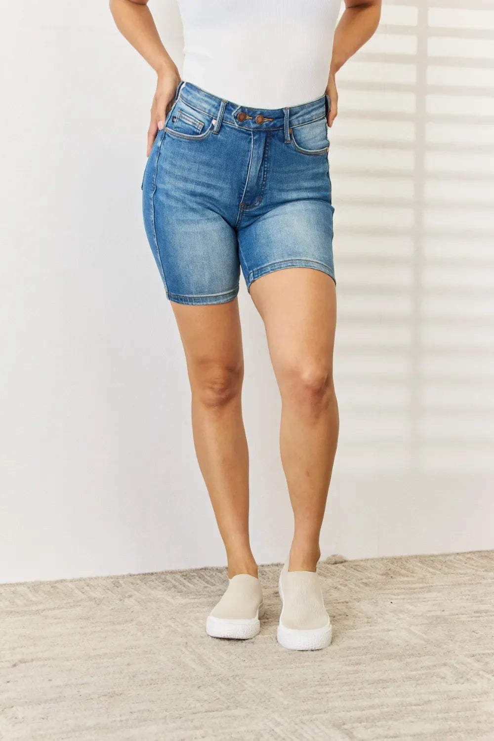 Woman wearing high-waisted denim bermuda shorts and white slip-on shoes indoors