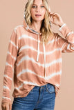 Woman wearing a tie-dye hooded sweatshirt with drawstrings and blue jeans, against beige background
