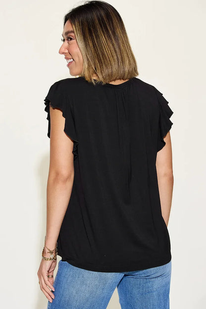 Woman wearing black flutter sleeve blouse and blue jeans, back view, neutral background