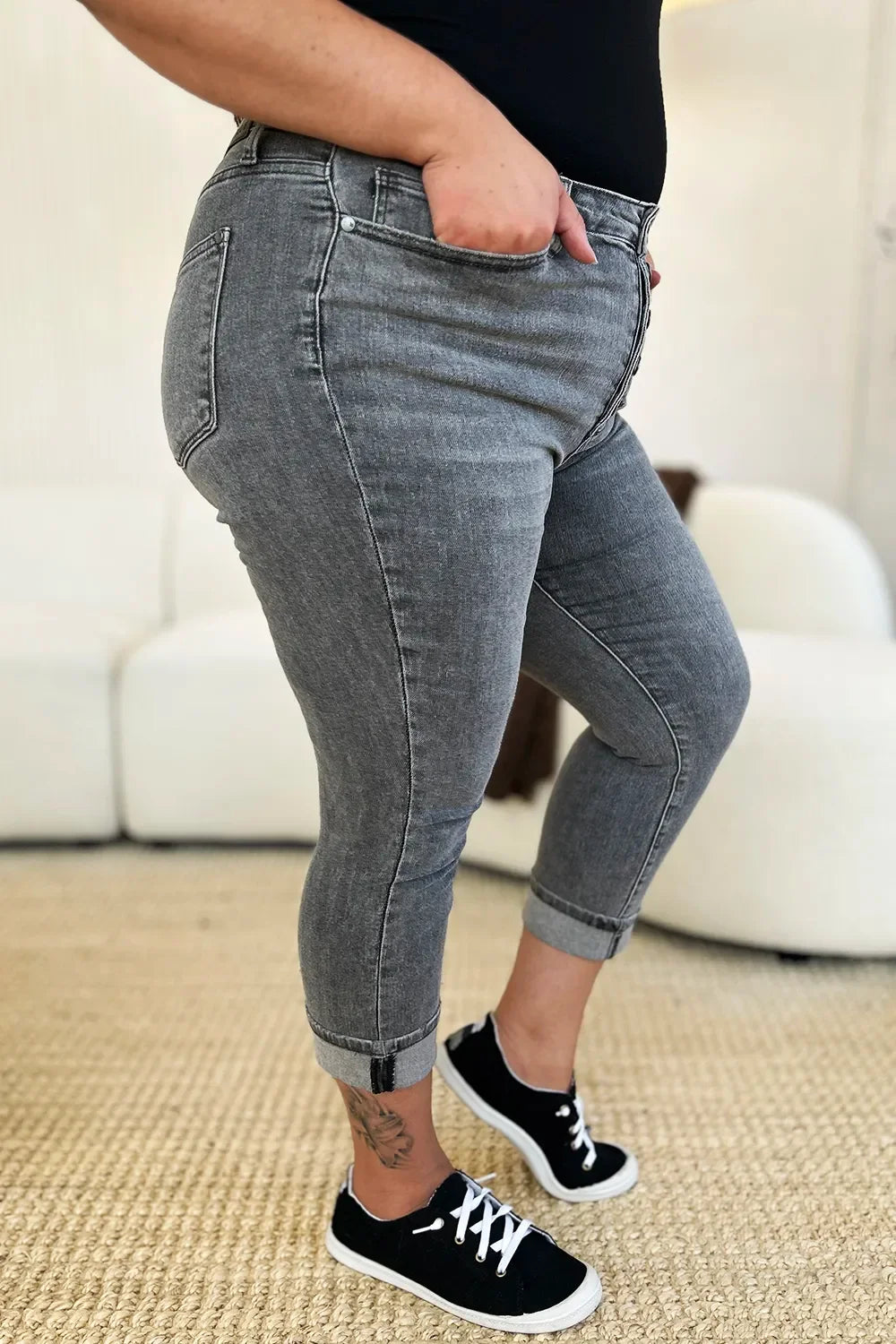 Woman wearing grey cropped skinny jeans with rolled cuffs and black sneakers indoors