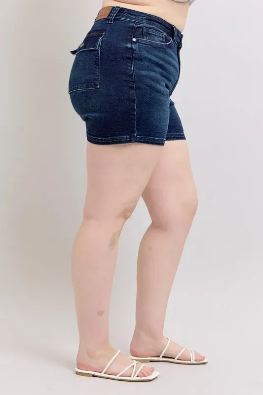 Side view of woman wearing dark wash denim shorts and white sandals on light background