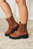 Brown leather ankle boots with side zippers and chunky black platform soles on a textured rug.
