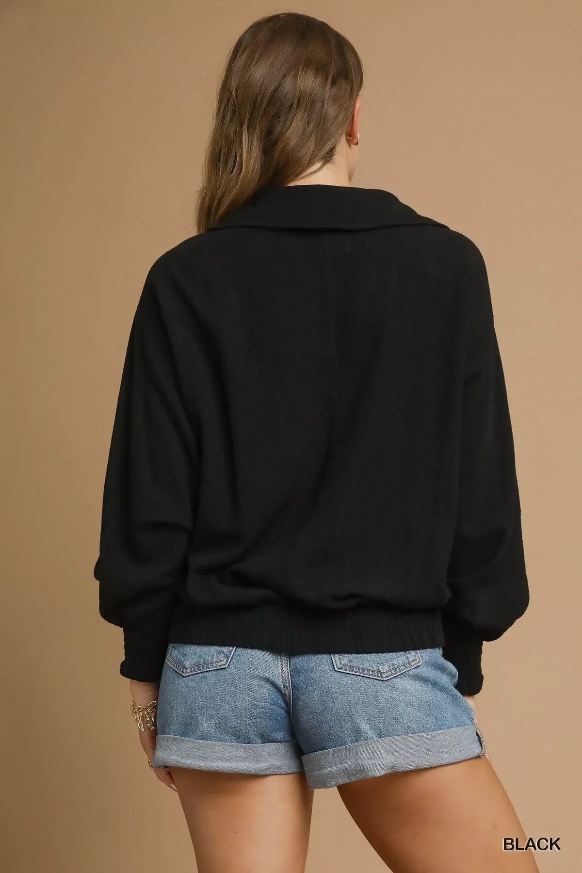 Woman wearing a black relaxed sweater and rolled denim shorts, back view, neutral background.
