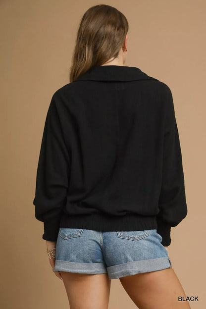 Woman wearing a black relaxed sweater and rolled denim shorts, back view, neutral background.
