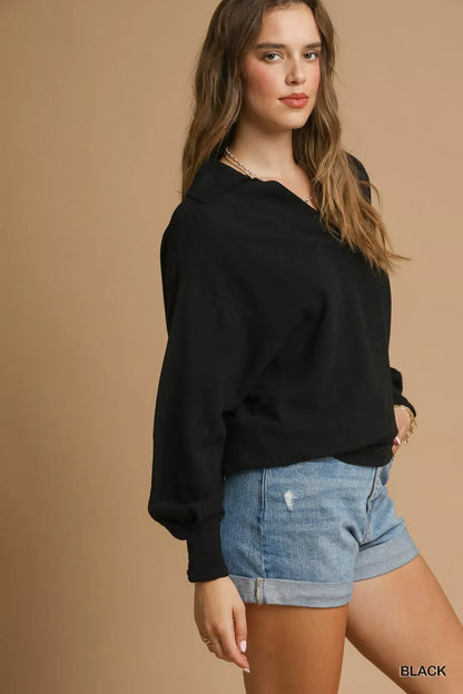 Woman wearing a black collared long sleeve top with denim high-waisted shorts on beige background.