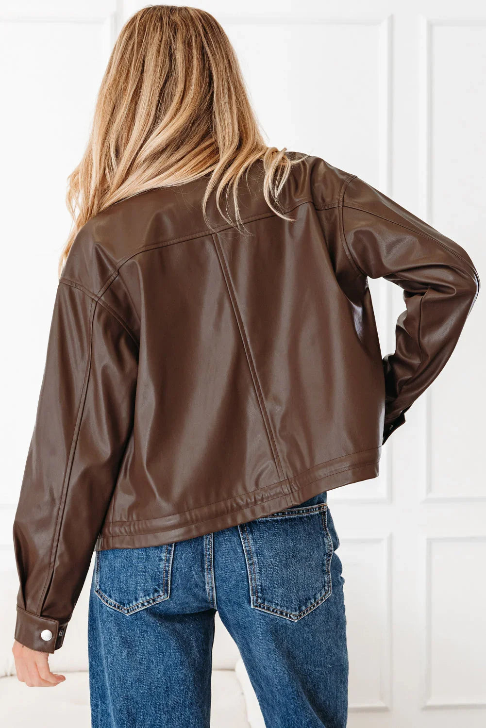Woman in brown faux leather jacket and blue jeans, seen from the back indoors
