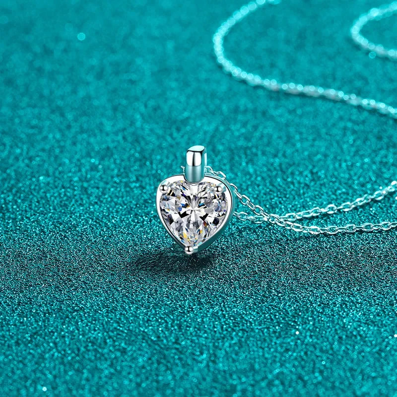Heart-shaped crystal pendant necklace on a silver chain against teal background