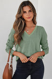 Woman wearing a green striped long sleeve V-neck top with casual jewelry and a brown handbag.