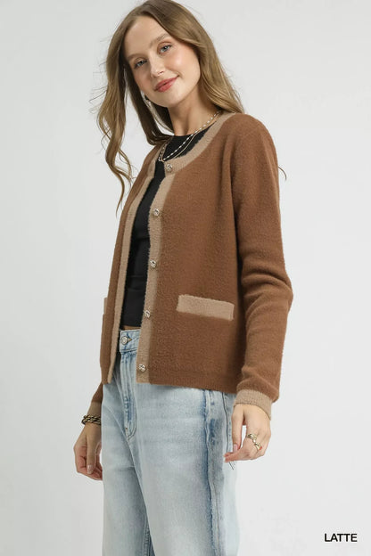 Woman wearing a brown and beige cardigan, black top, and light wash jeans in a studio setting.