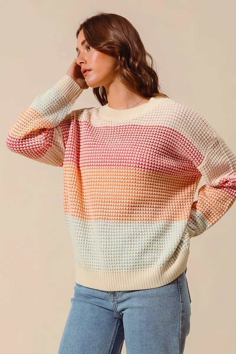 Woman wearing a pastel striped knit sweater with relaxed fit and light blue jeans