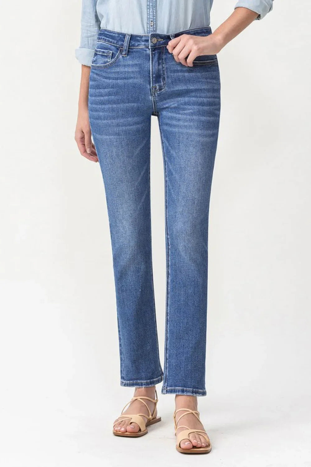 Woman wearing straight leg blue jeans and strappy sandals on a white background