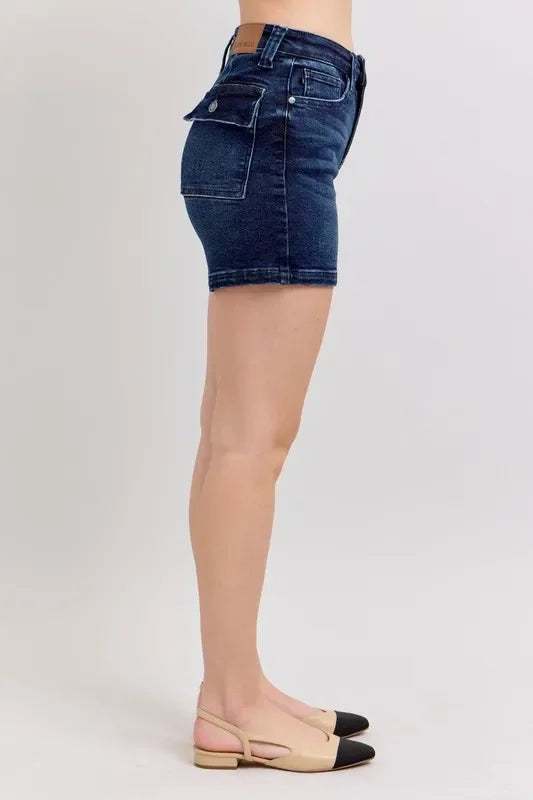 Side view of woman wearing dark wash denim shorts with utility pocket and beige slingback flats