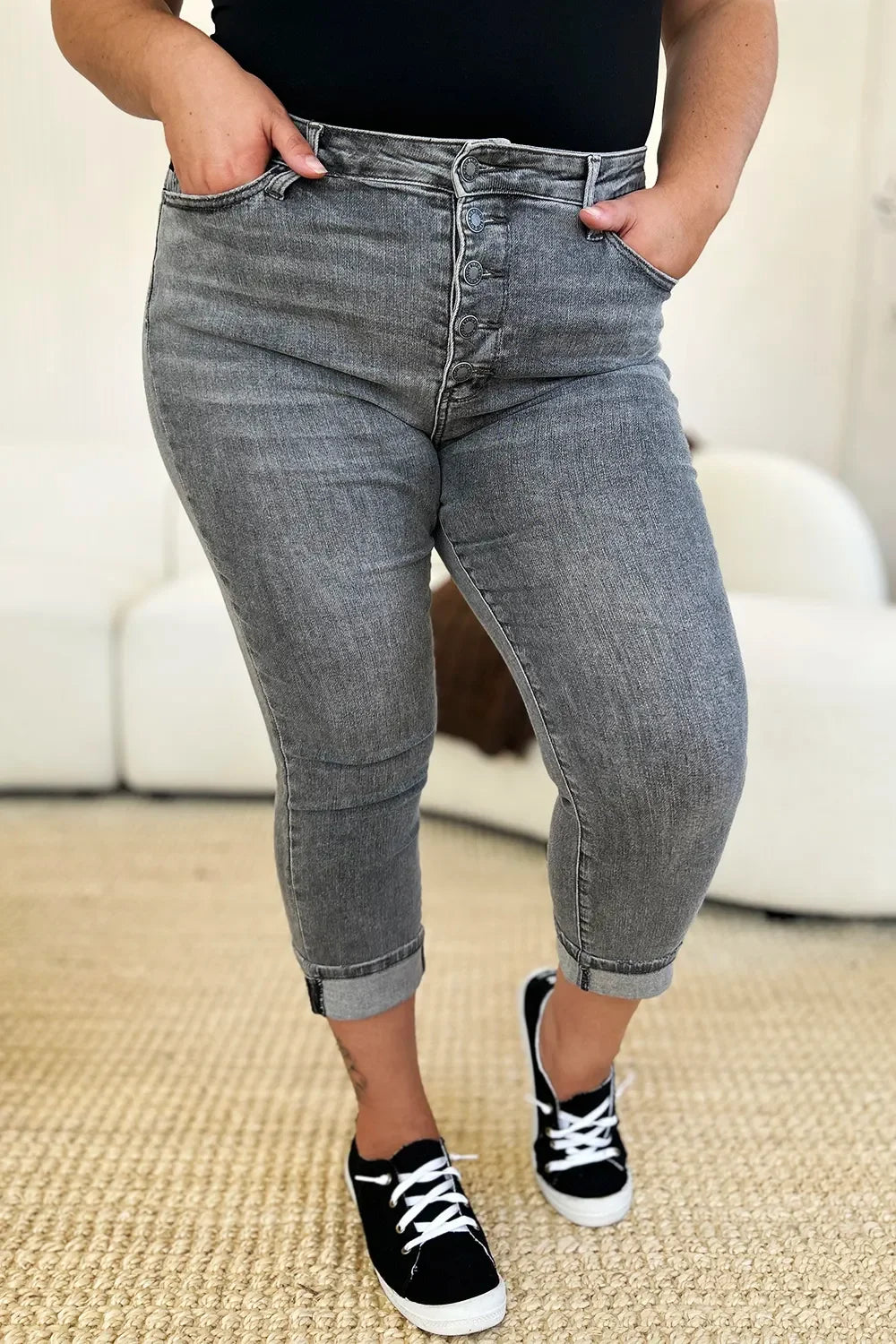 Woman wearing high-waisted grey cropped jeans with button fly and black sneakers indoors.