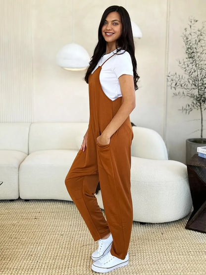 Woman wearing rust brown relaxed jumpsuit over white t-shirt, white sneakers, modern living room setting.