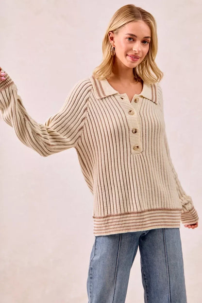 Woman in a cream ribbed knit pullover sweater with buttons and blue jeans on neutral background