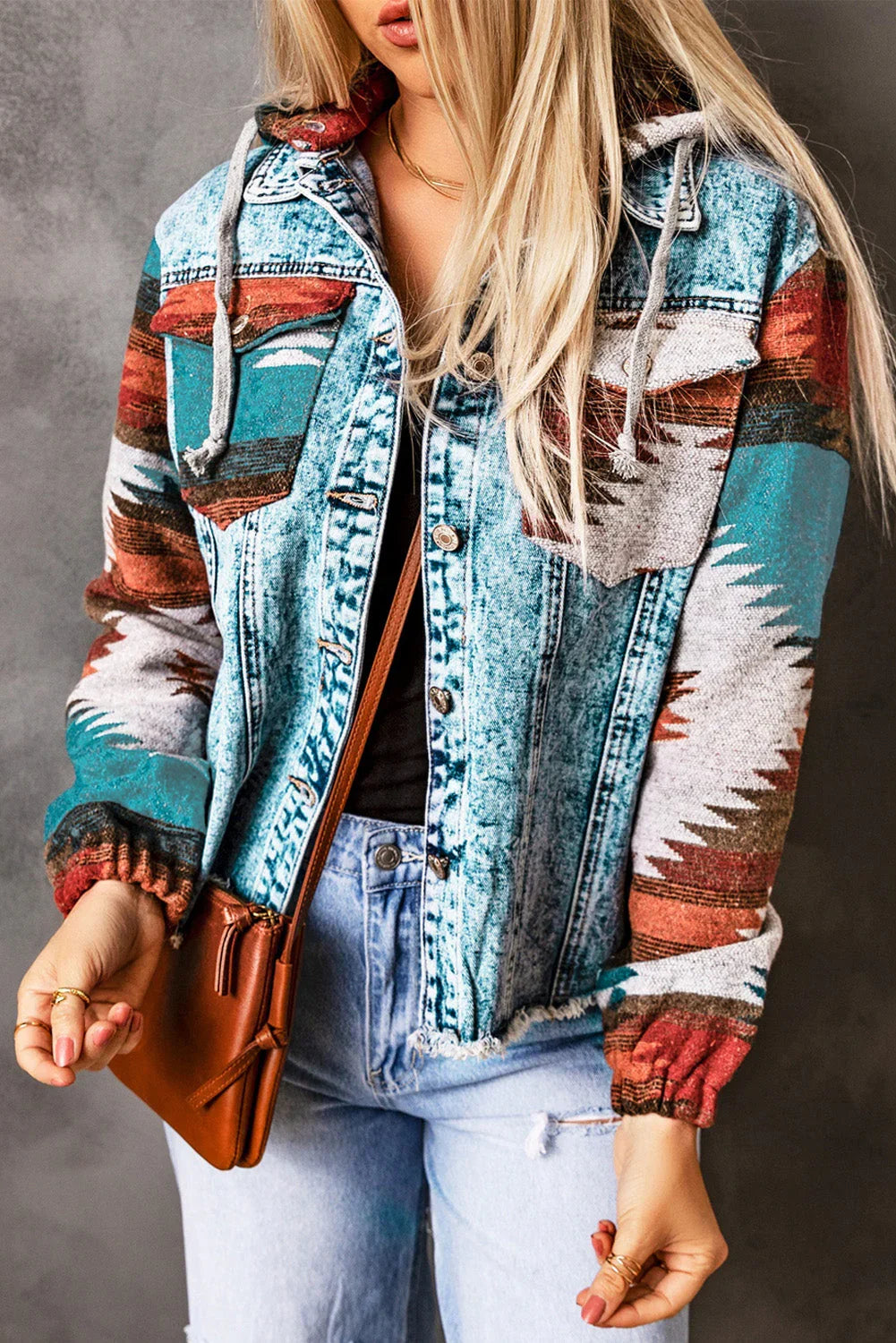 Woman wearing a denim jacket with colorful geometric sleeves, light jeans, and a brown crossbody bag.