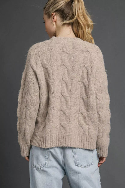 Back view of woman in cable-knit stone-colored sweater and light wash jeans
