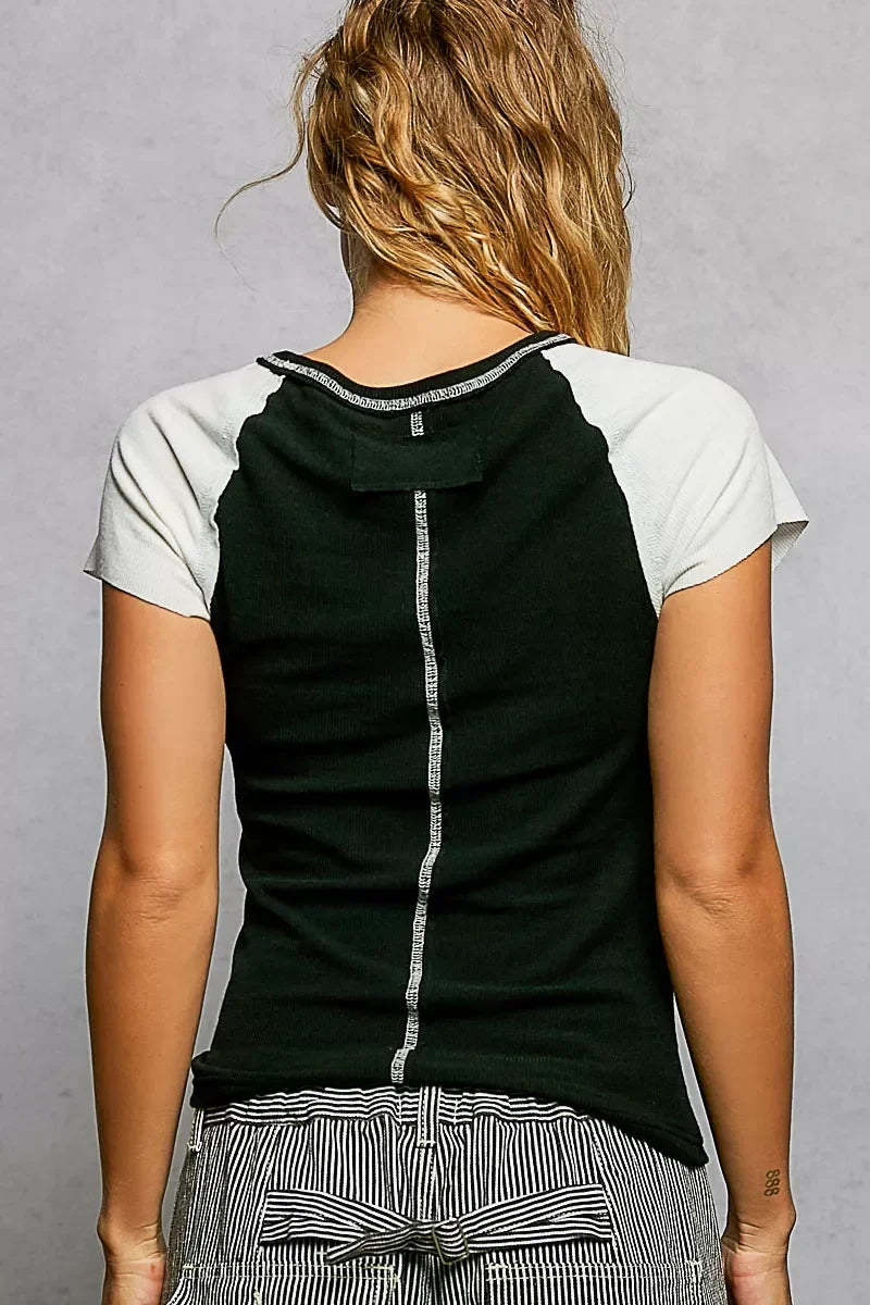 Woman wearing a black short sleeve top with white sleeves and striped high-waist pants, back view.