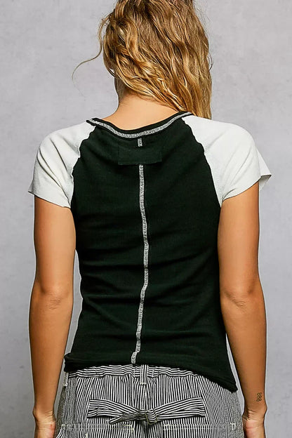 Woman wearing a black short sleeve top with white sleeves and striped high-waist pants, back view.