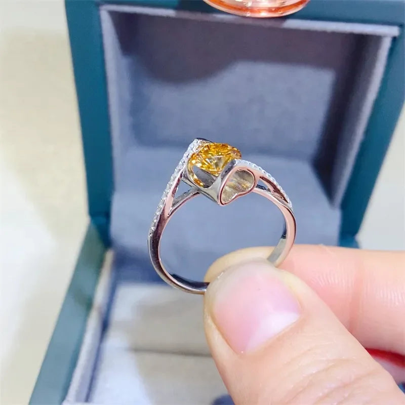 Silver ring with yellow gemstone in a heart-shaped setting, displayed in a jewelry box