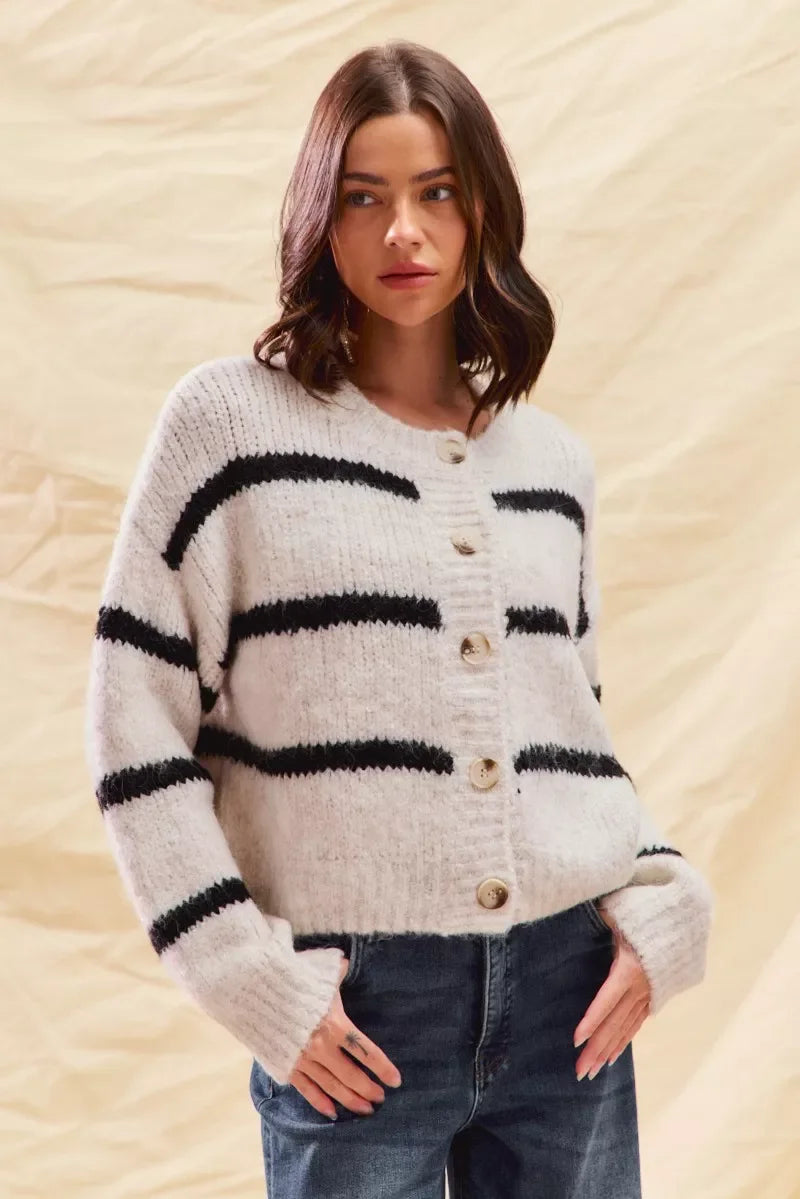 Woman wearing a cozy white striped cardigan sweater with button front and casual blue jeans.