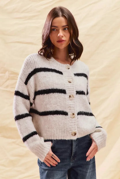 Woman wearing a cozy white striped cardigan sweater with button front and casual blue jeans.