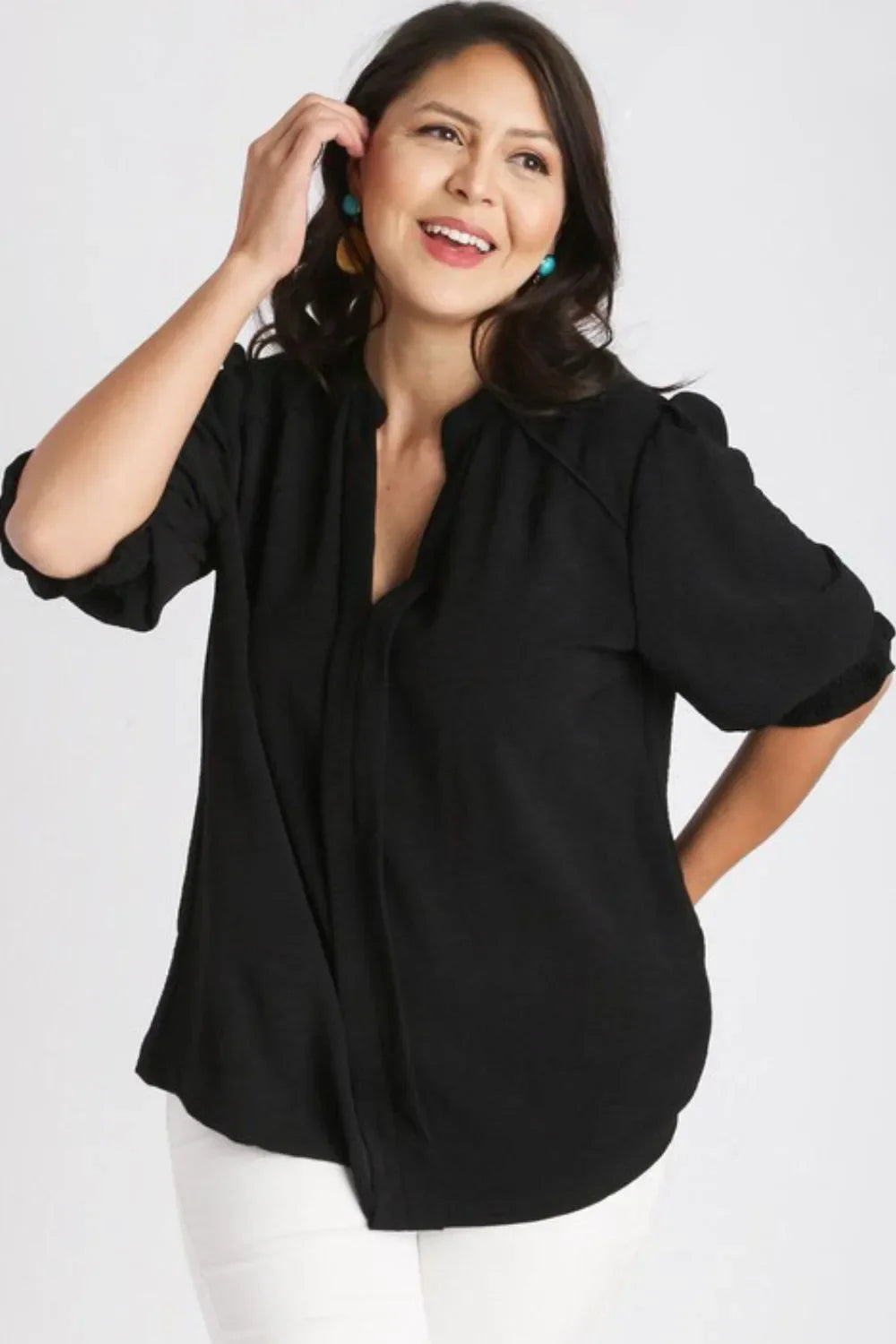 Woman wearing a loose black blouse with quarter sleeves and white pants, posing against a white background.