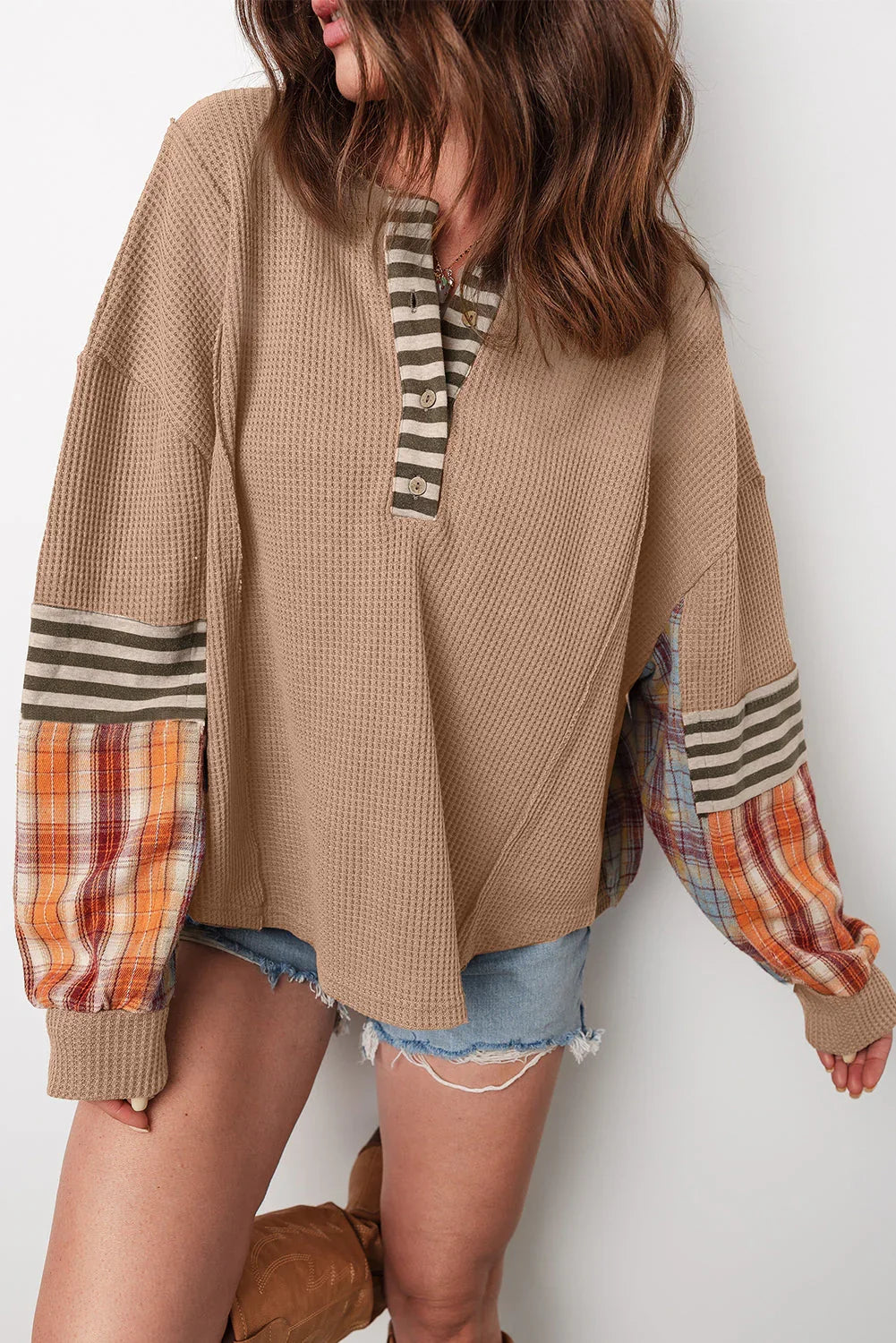 Textured beige henley top with striped collar, plaid and striped sleeves, paired with denim shorts.
