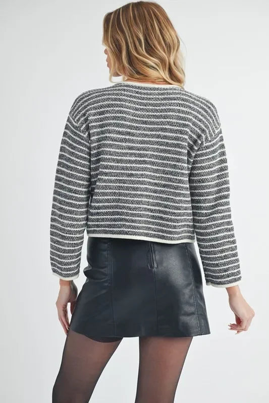 Woman wearing black faux leather mini skirt, striped knit sweater, sheer tights, back view