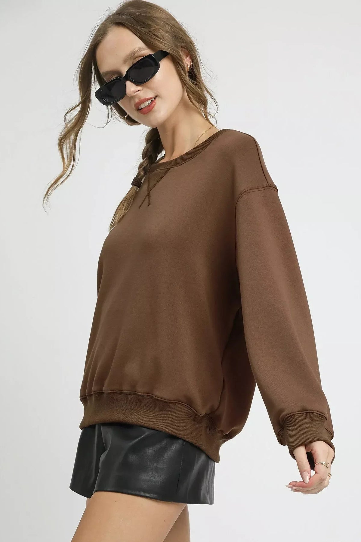 Woman wearing mocha brown oversized sweatshirt and black faux leather shorts