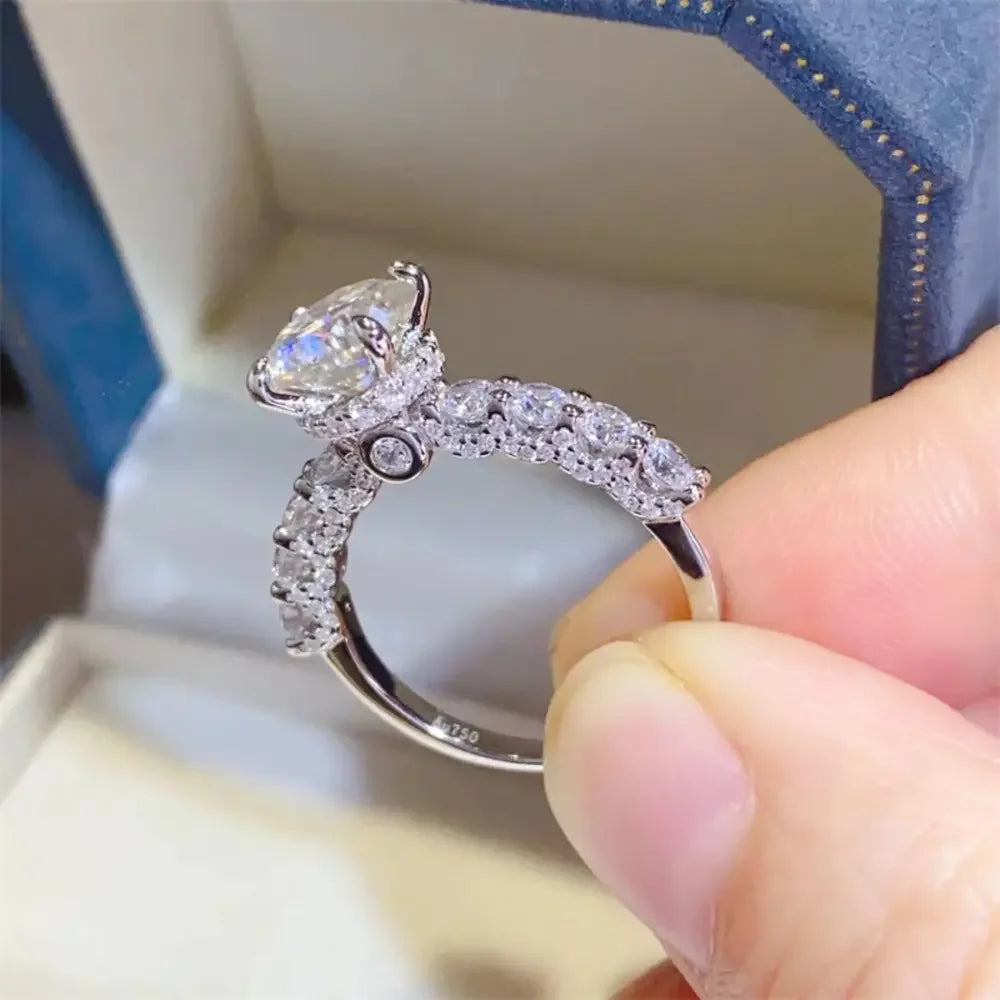Hand holding a silver ring with a large oval gemstone and pavé diamond band in jewelry box
