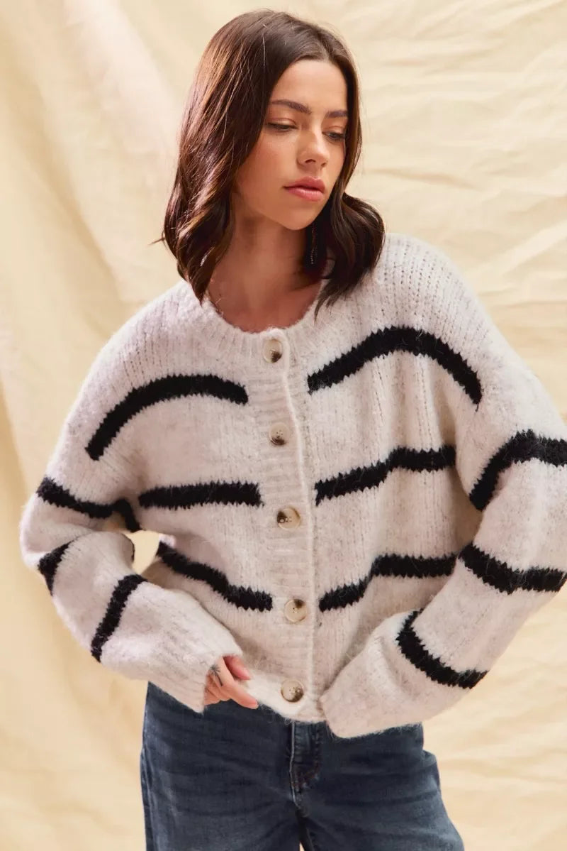 Woman wearing fuzzy white cardigan with black stripes and large buttons, paired with jeans