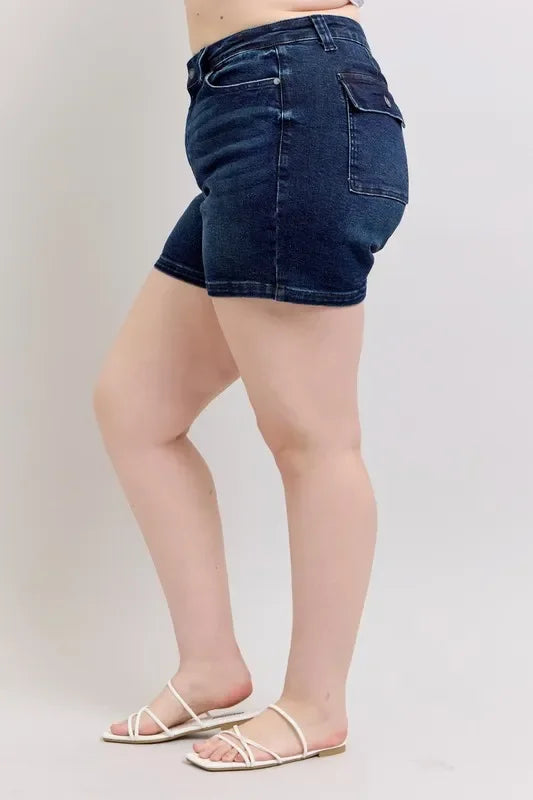 Woman wearing dark denim high-waisted shorts and white sandals, side view.