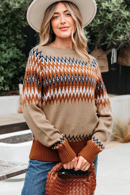 Woman in beige and rust zigzag knit sweater, wide-brim hat, holding brown woven bag outdoors