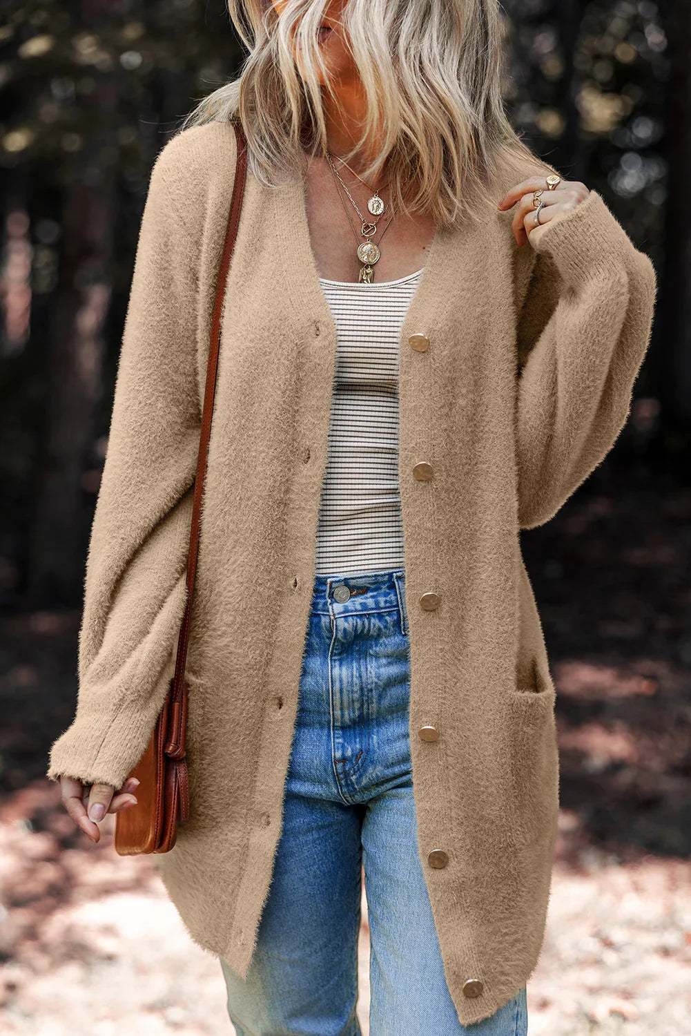 Woman outdoors wearing a tan oversized cardigan, striped top and blue jeans with a brown bag.
