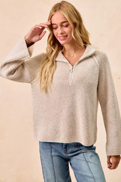Woman wearing a beige ribbed quarter-zip sweater and light blue jeans