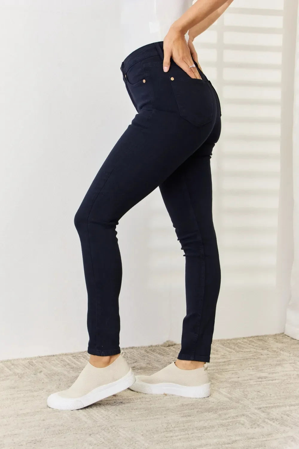 Woman wearing dark skinny jeans and slip-on shoes in a minimalist indoor setting