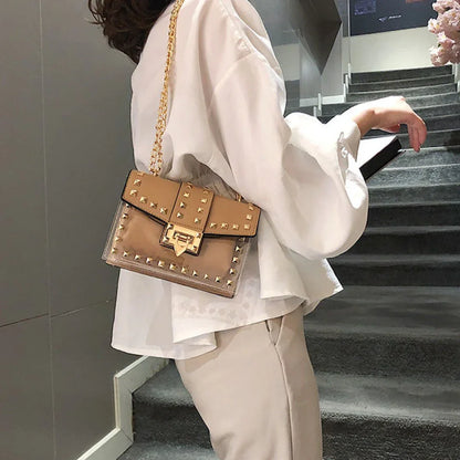 Tan clear shoulder bag with gold chain and stud detailing, worn by woman in white blouse