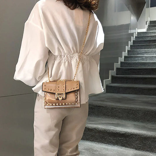 Clear tan studded shoulder bag with gold chain strap, styled on woman in modern setting