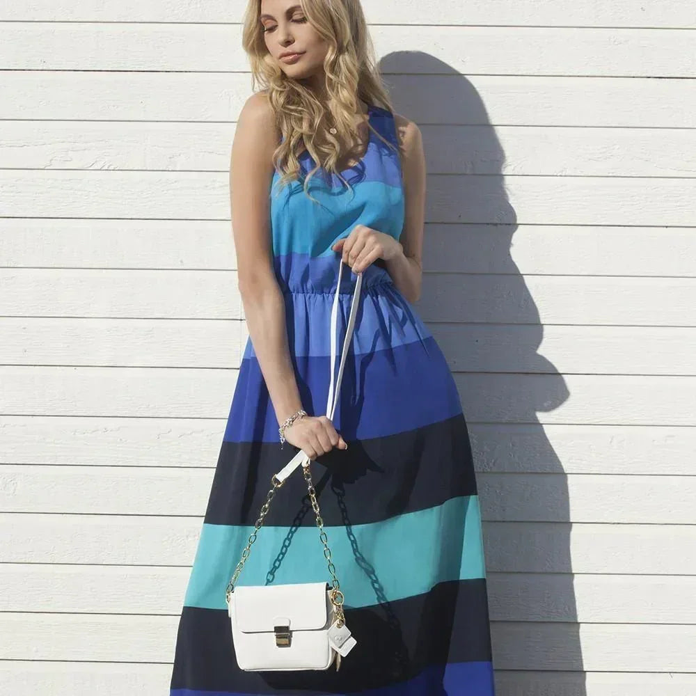 Woman in striped blue maxi dress holding a small white leather handbag with gold chain
