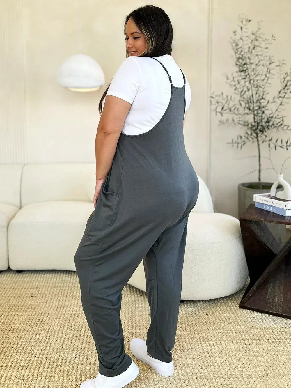 Woman in gray relaxed-fit overalls and white t-shirt standing in modern living room