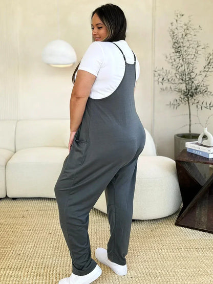 Woman in gray relaxed-fit overalls and white t-shirt standing in modern living room