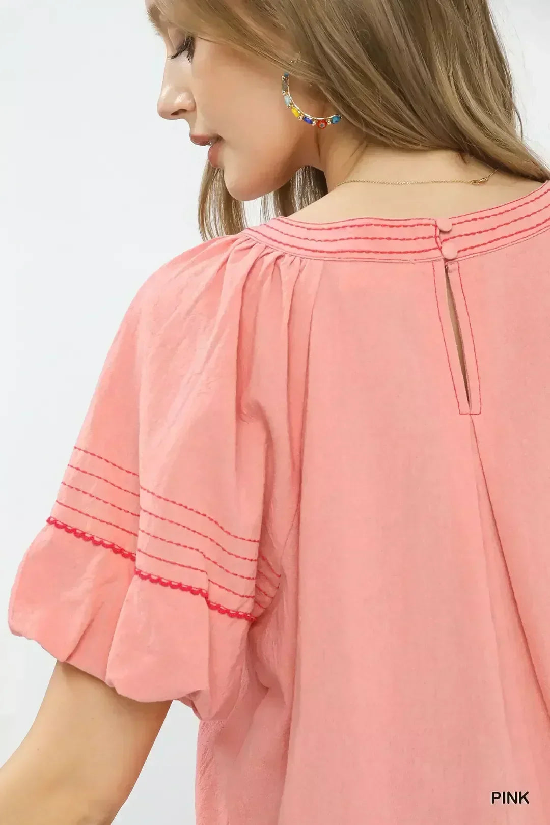 Back view of woman in pink blouse with gathered sleeves and delicate red stitching.